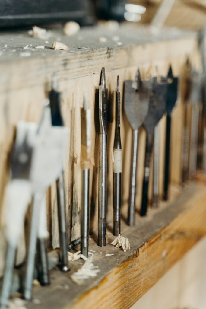 Close-up of various drill bits on a wooden shelf in a workshop setting.